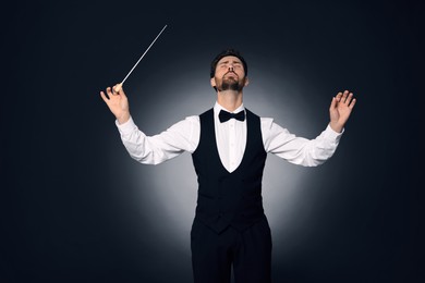 Professional conductor with baton on dark background