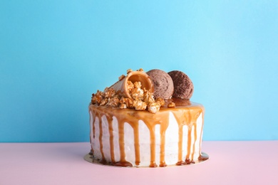 Delicious homemade cake with caramel sauce and popcorn on table against color background