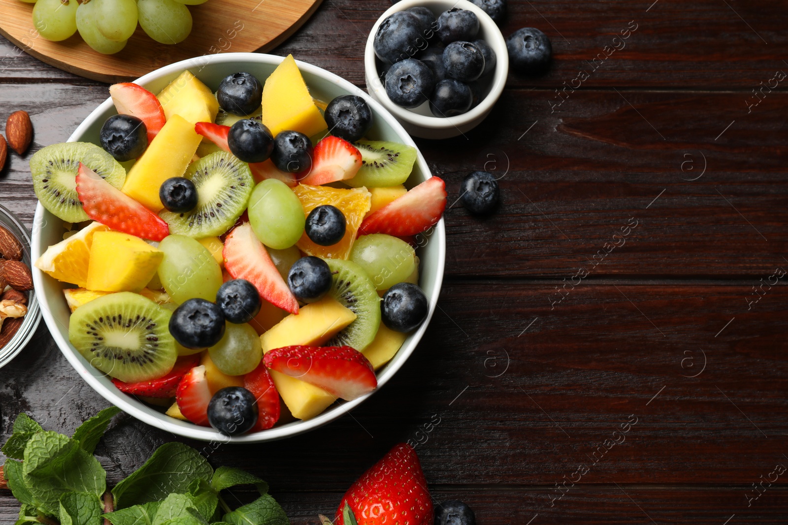 Photo of Tasty fruit salad in bowl and ingredients on wooden table, flat lay. Space for text