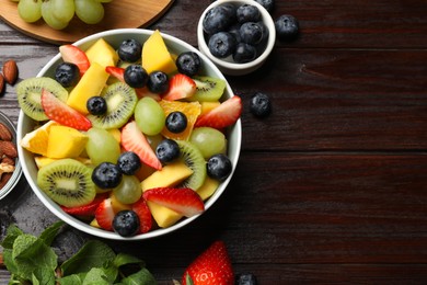 Tasty fruit salad in bowl and ingredients on wooden table, flat lay. Space for text