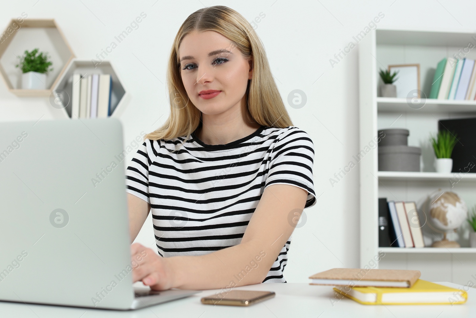 Photo of Home workplace. Woman working on laptop at white desk in room