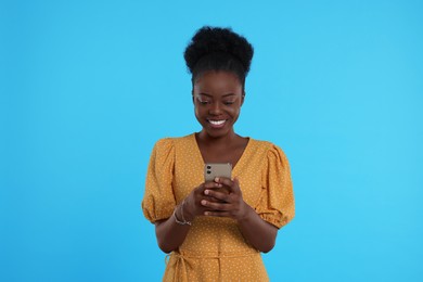 Happy young woman with smartphone on light blue background