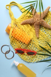 Photo of String bag, different beach accessories and palm leaves on light blue background, flat lay