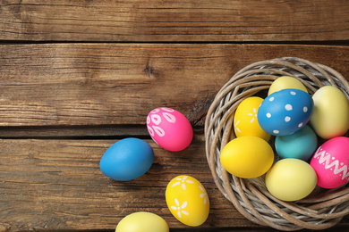 Photo of Colorful Easter eggs in decorative nest on wooden background, flat lay. Space for text