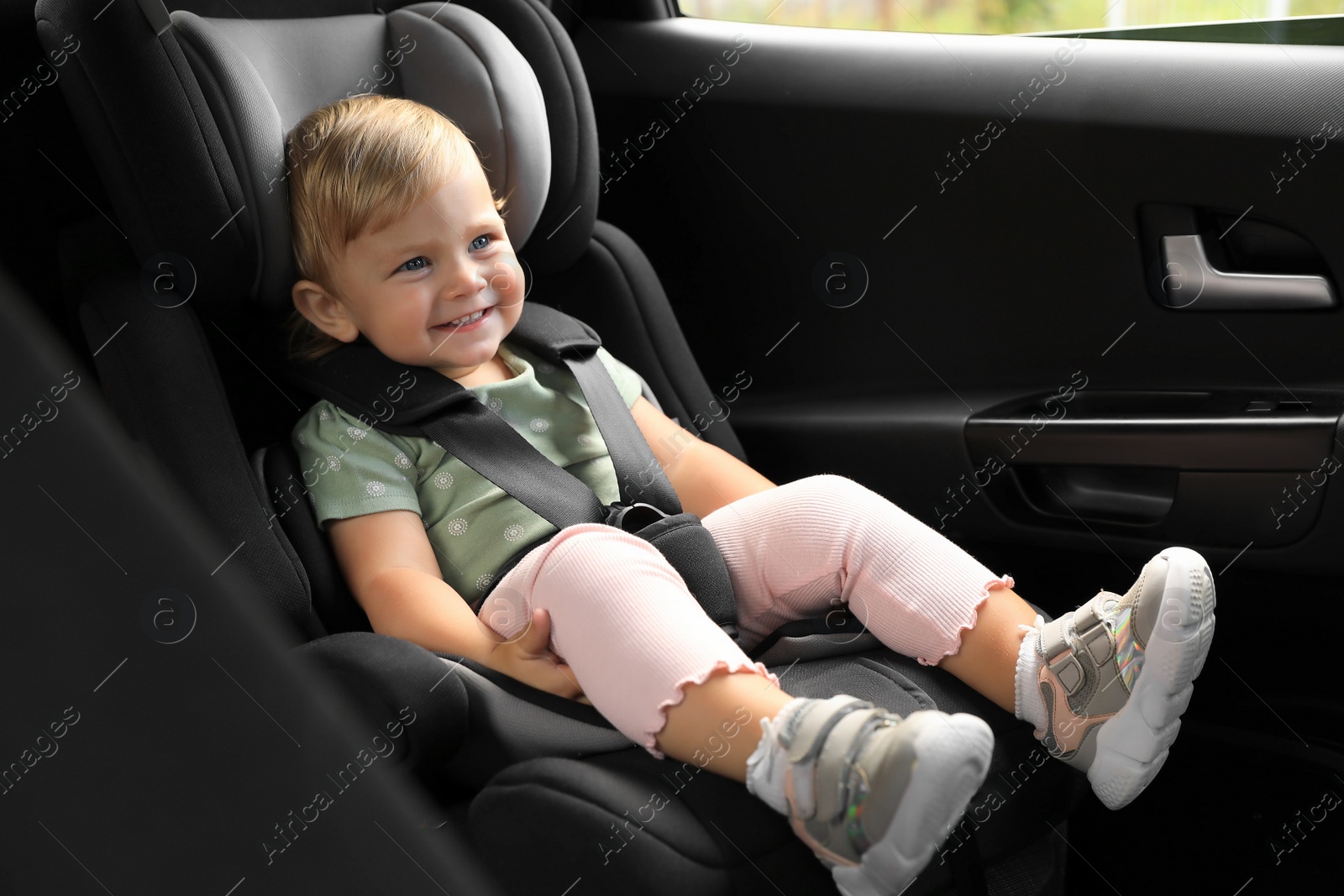 Photo of Cute little girl sitting in child safety seat inside car