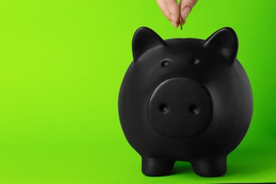 Woman putting coin into piggy bank on green background, closeup. Space for text