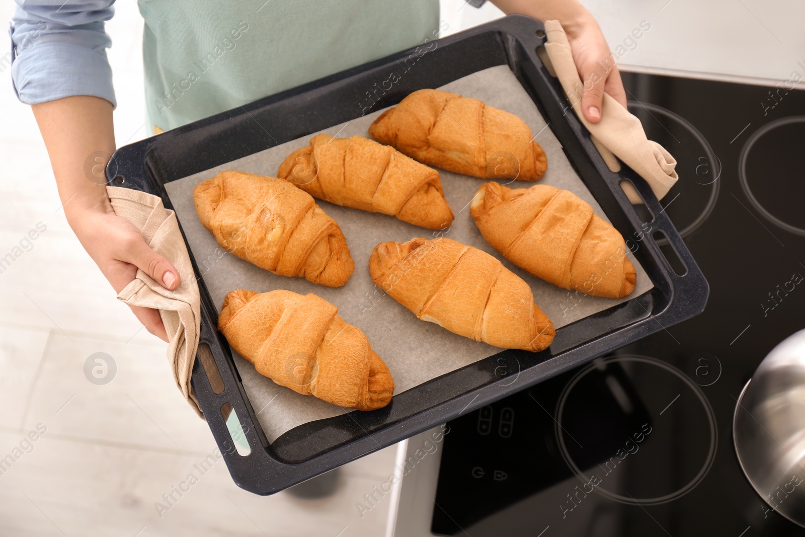 Photo of Woman holding baking tray with delicious croissants in kitchen, closeup
