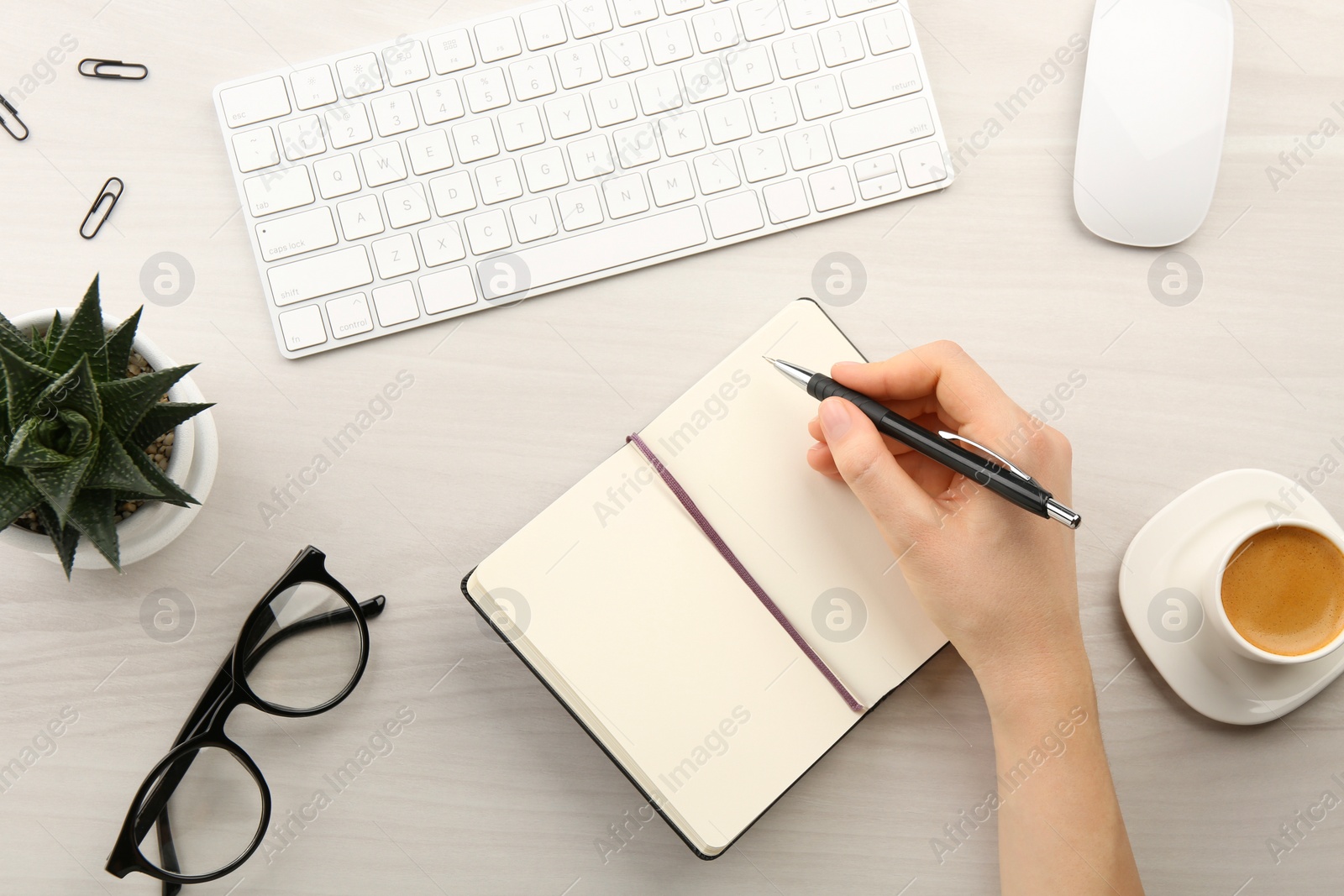 Photo of Woman writing in notebook at light wooden table, top view