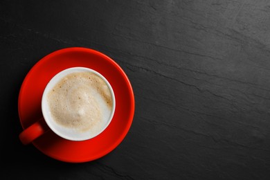 Red cup with aromatic cappuccino on black textured table, top view. Space for text