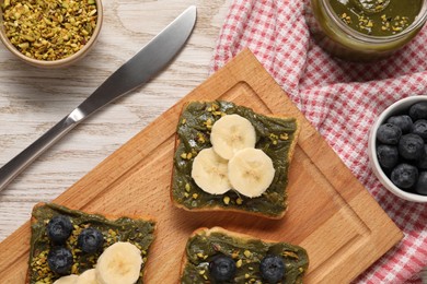 Photo of Toasts with tasty pistachio butter, banana slices, blueberries and nuts on white wooden table, flat lay