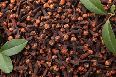 Photo of Many aromatic cloves and green leaves as background, top view. Space for text