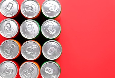 Photo of Energy drink in cans on red background, top view. Space for text