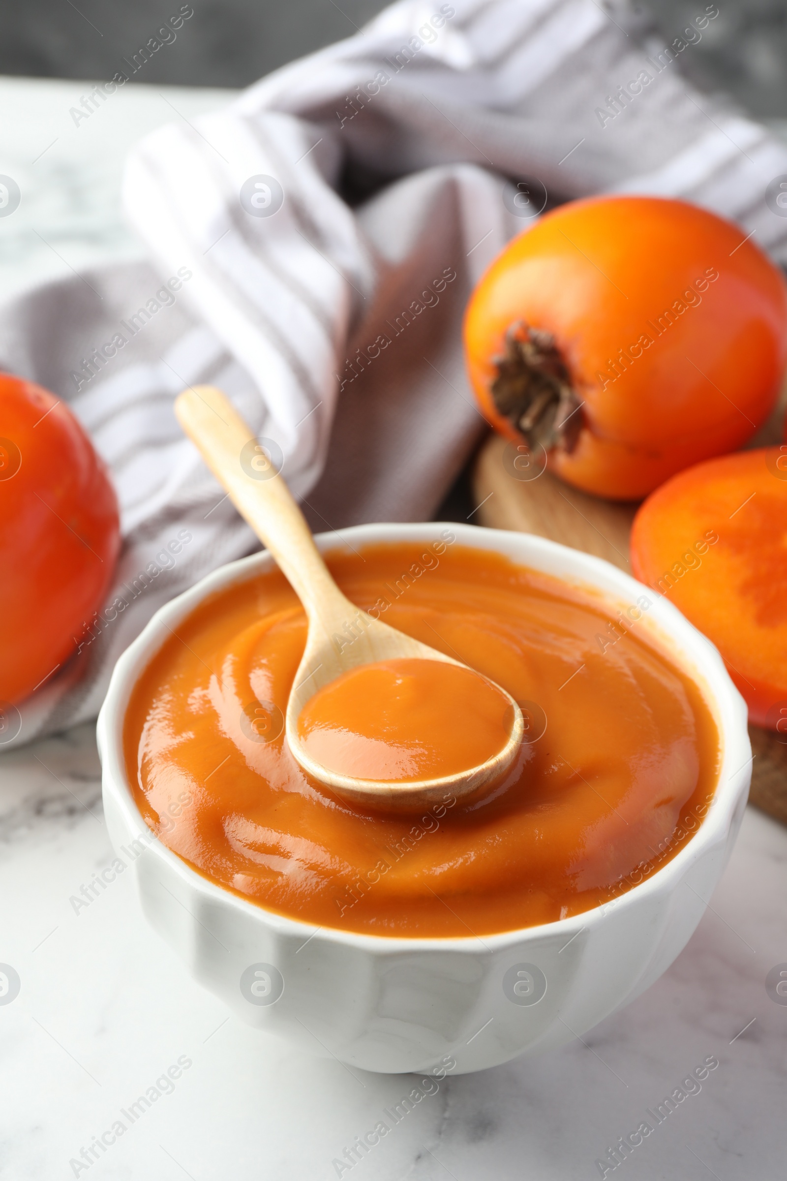 Photo of Delicious persimmon jam and fresh fruits on table, closeup