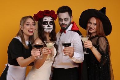Photo of Group of people in scary costumes with cocktails on orange background. Halloween celebration