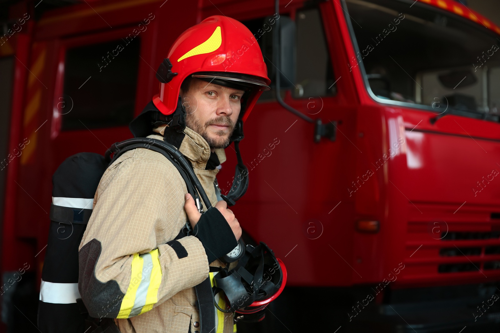 Photo of Portrait of firefighter in uniform near red fire truck at station