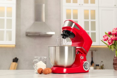 Photo of Modern red stand mixer, eggs and container with flour on white marble table in kitchen, space for text