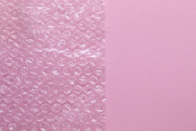 Photo of Transparent bubble wrap on pink background, top view. Space for text