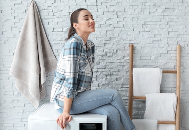 Photo of Young woman sitting on washing machine in laundry room