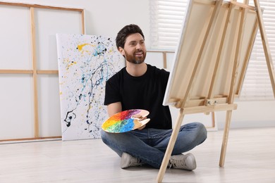 Photo of Man painting in studio. Using easel to hold canvas