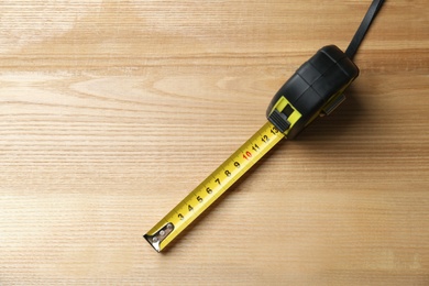 Photo of Tape measure on wooden background, top view. Construction tool