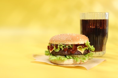 Photo of Burger with delicious patty and soda drink on yellow background, space for text