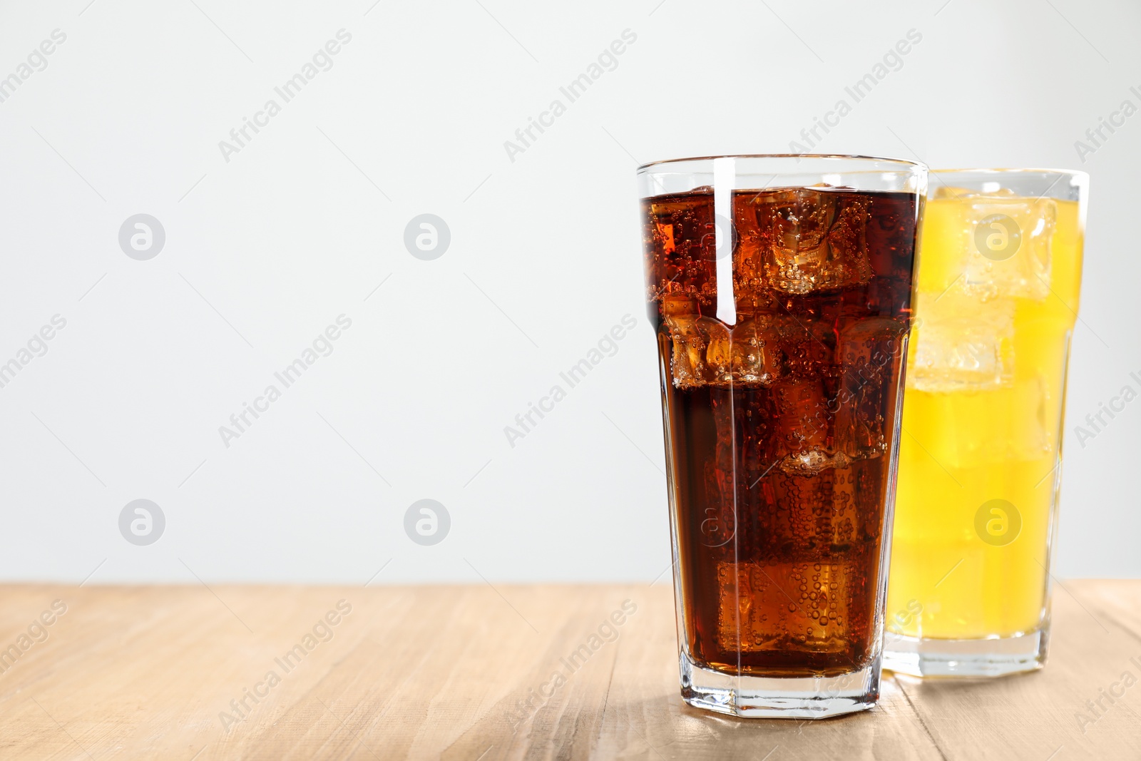 Photo of Glasses of different refreshing soda water with ice cubes on wooden table, space for text