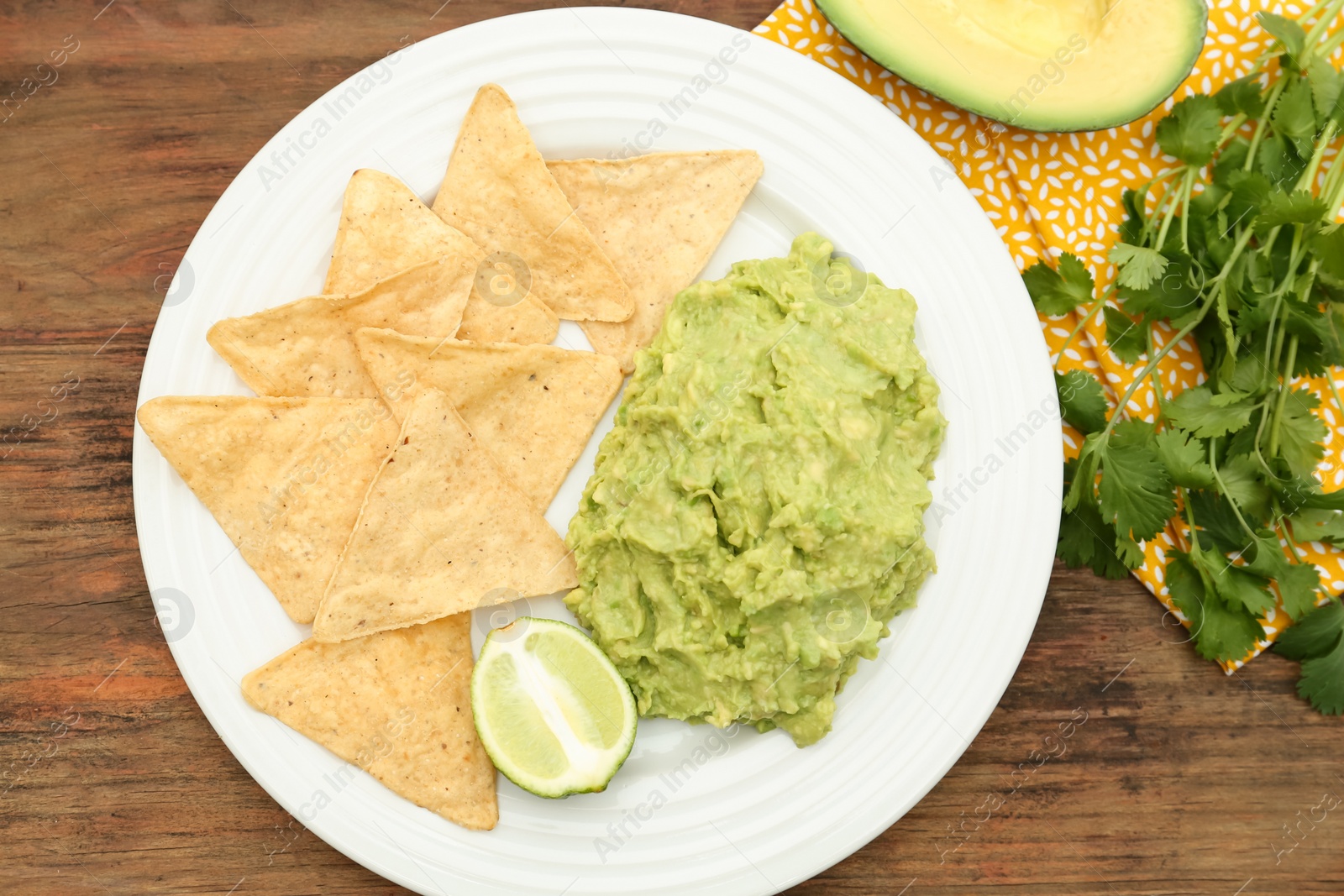 Photo of Delicious guacamole made of avocados, nachos and lime on wooden table, flat lay