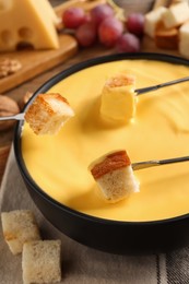 Photo of Dipping pieces of bread into tasty cheese fondue at table, closeup