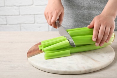 Photo of Woman cutting fresh green celery at white wooden table indoors, closeup