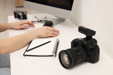 Photo of Photographer working on computer at white table with camera indoors, closeup