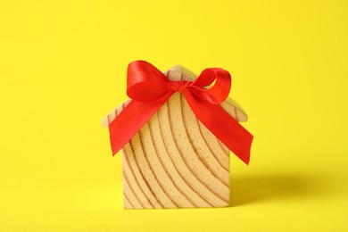 Wooden house model with red bow on yellow background, closeup. Housewarming party