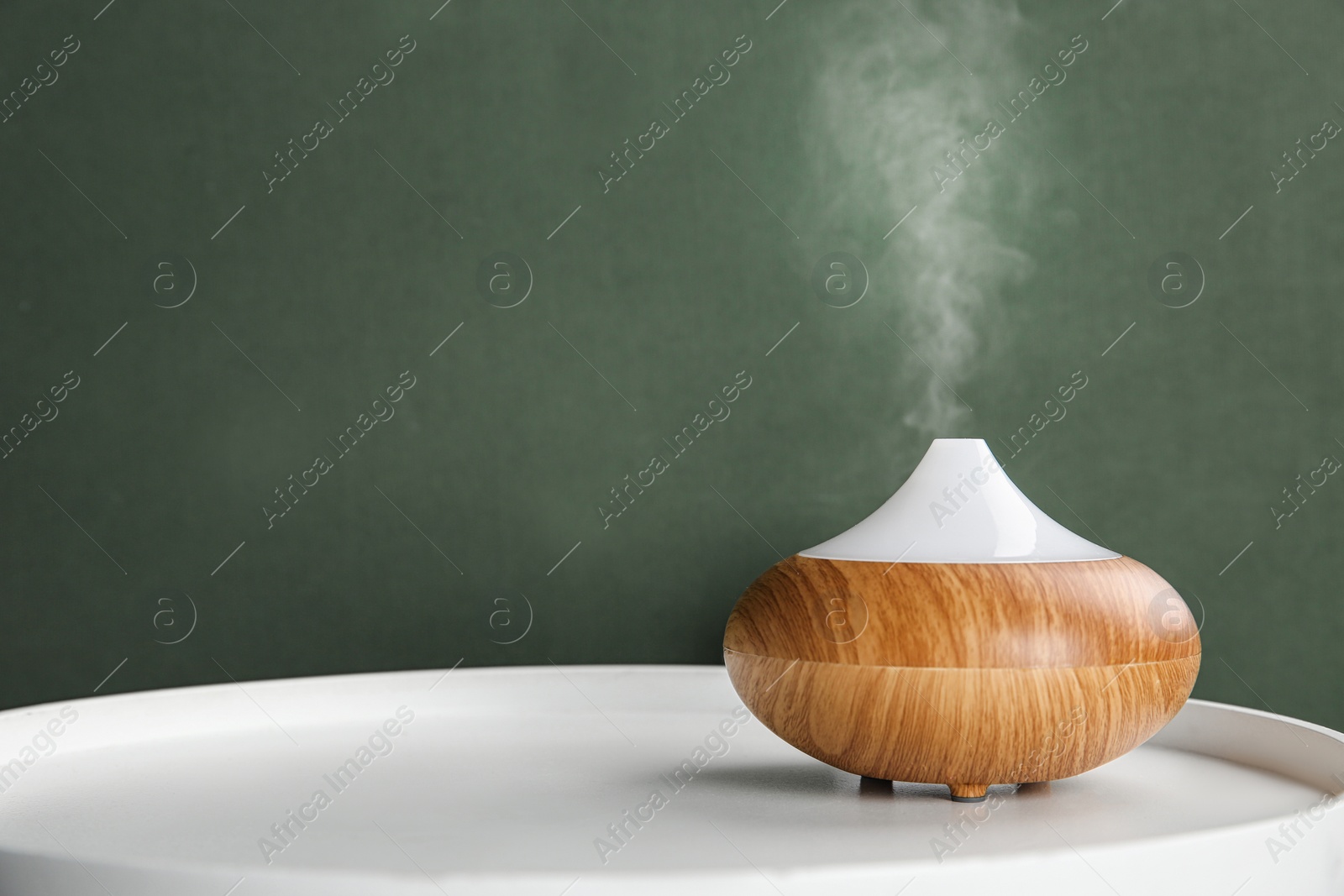 Photo of Modern essential oil diffuser on white table against green background. Space for text