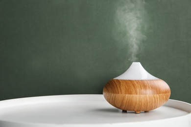 Photo of Modern essential oil diffuser on white table against green background. Space for text