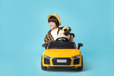 Photo of Little boy with his dog in toy car on light blue background