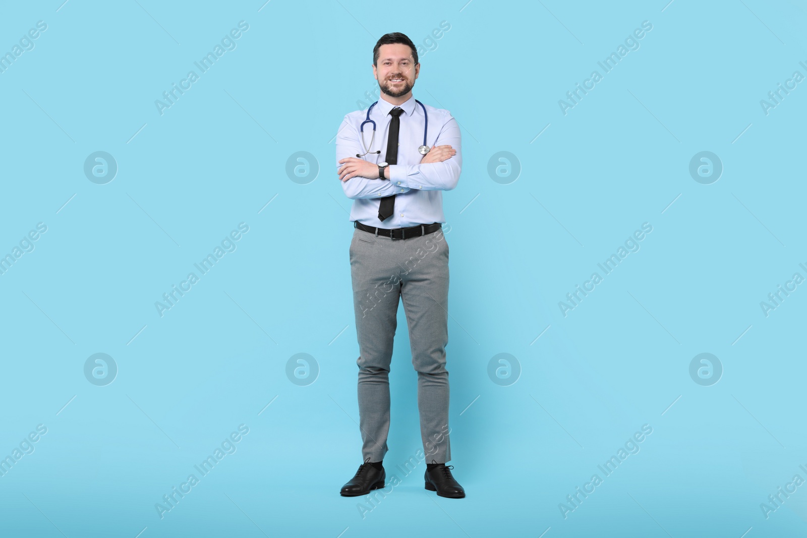 Photo of Smiling doctor with stethoscope on light blue background