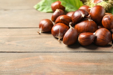 Photo of Fresh sweet edible chestnuts on wooden table, closeup. Space for text
