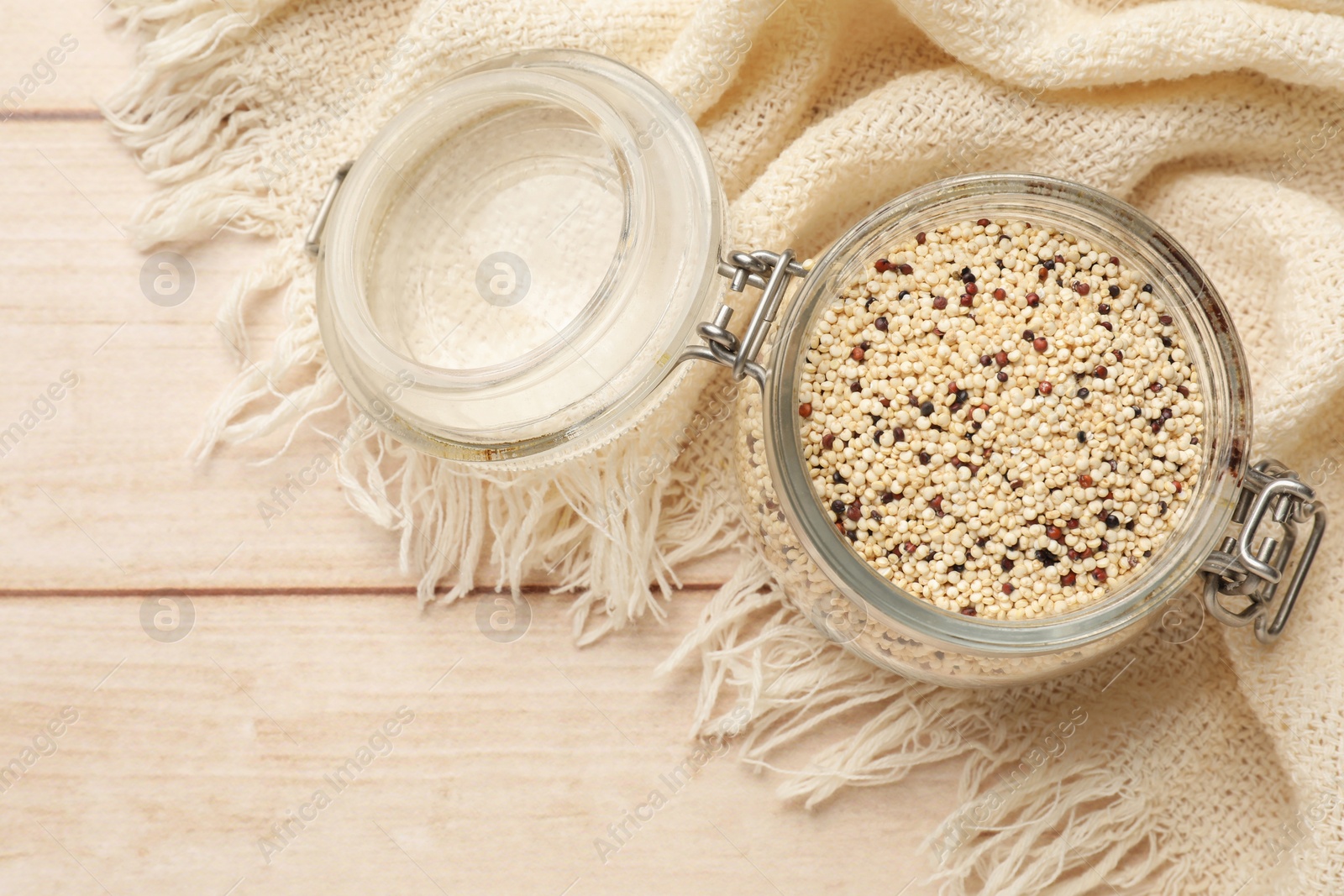 Photo of Raw quinoa seeds in jar on wooden table, top view. Space for text