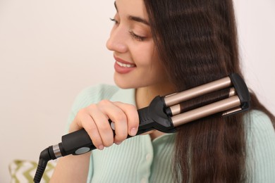 Photo of Young woman using modern curling iron on light background, closeup