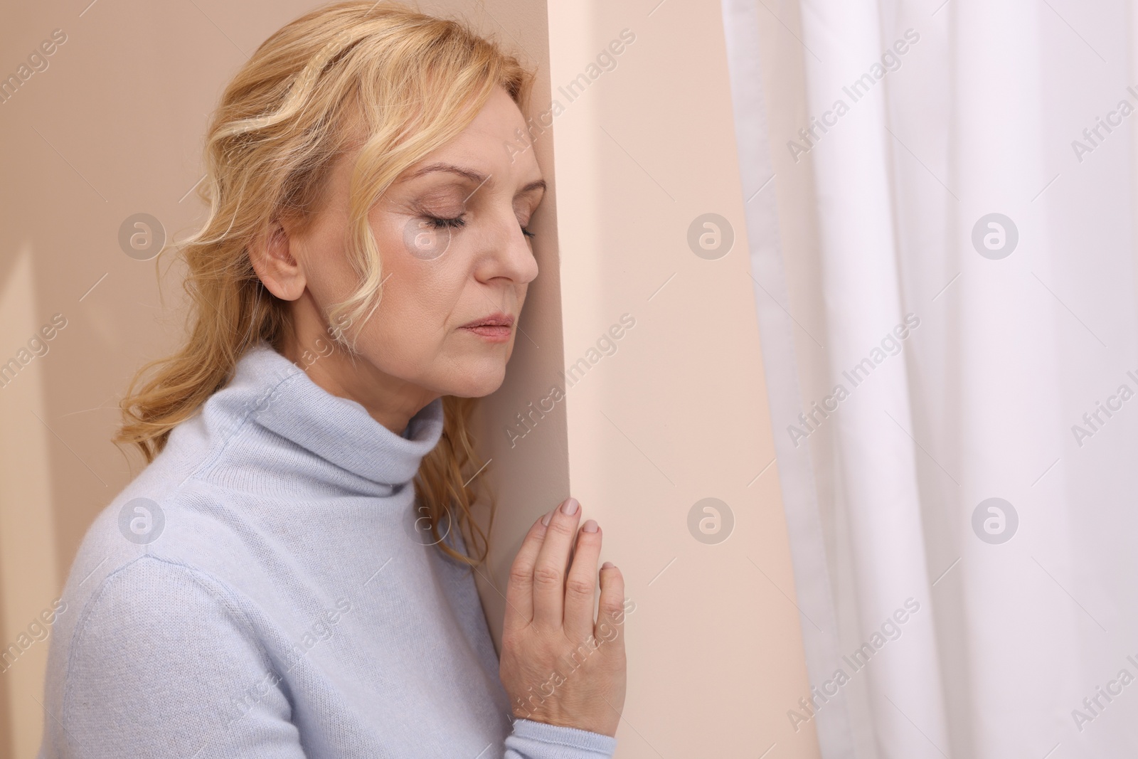 Photo of Upset middle aged woman near window at home. Loneliness concept