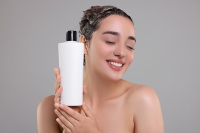 Photo of Washing hair. Portrait of beautiful happy woman with bottle on grey background