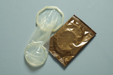 Photo of Unrolled female condom and package on light blue background, above view. Safe sex