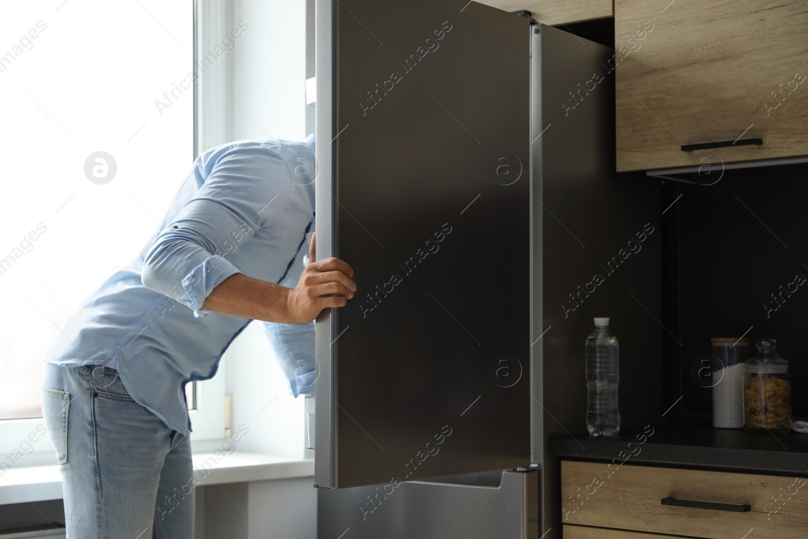 Photo of Man looking into refrigerator full of products in kitchen