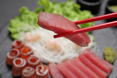 Chopsticks with tasty sashimi (piece of fresh raw tuna) against blurred background, closeup