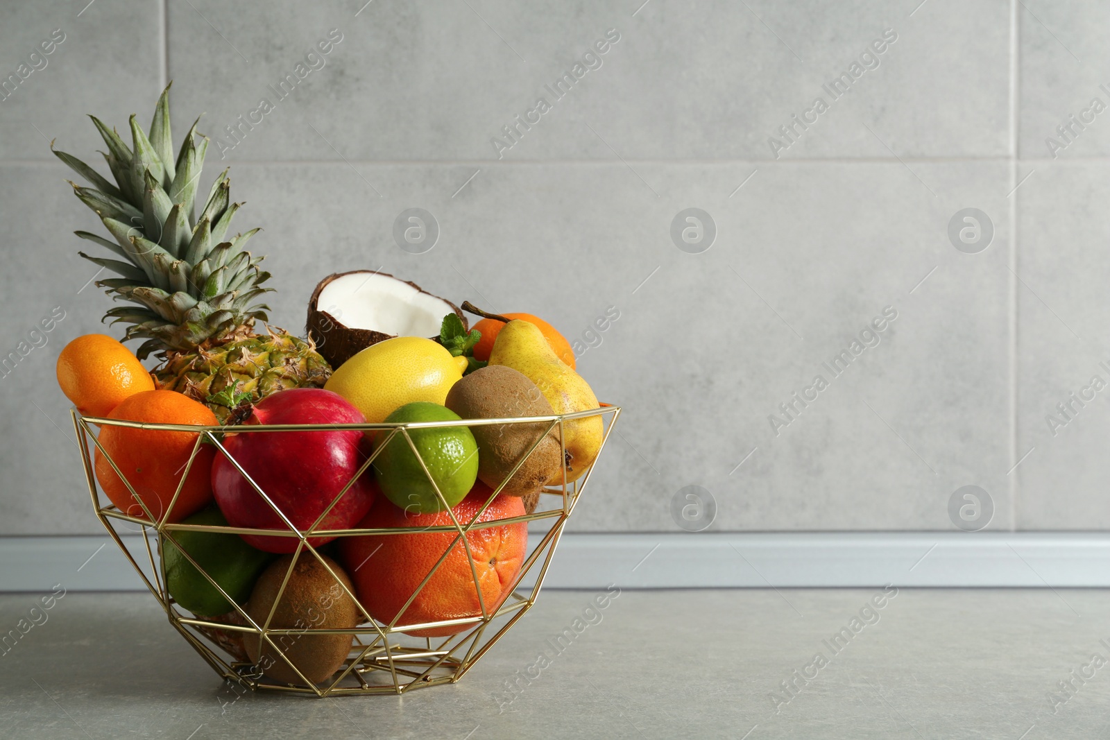 Photo of Metal basket with different ripe fruits on grey table. Space for text