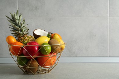 Metal basket with different ripe fruits on grey table. Space for text