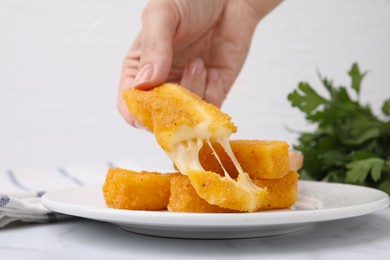 Photo of Woman taking tasty fried mozzarella stick from plate at table, closeup