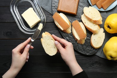 Photo of Making sandwich with quince paste. Woman spreading butter on bread at black wooden table, top view