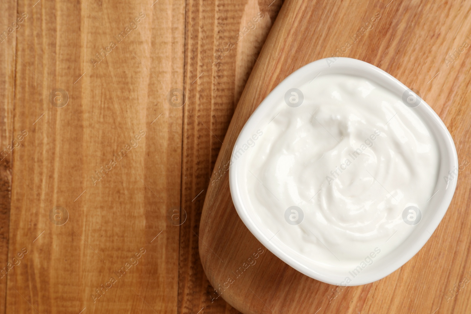 Photo of Bowl of fresh yogurt on wooden table, top view. Space for text