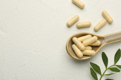 Vitamin capsules in spoon and leaves on white wooden table, flat lay. Space for text