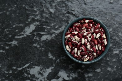 Photo of Bowl with dry kidney beans on black textured table, top view. Space for text